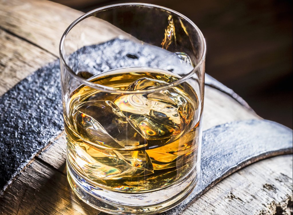 A glass of whiskey with ice on an old wooden barrel