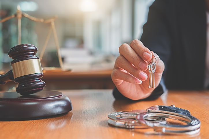 Close-Up Of Judge Holding Keys With Handcuffs On Table