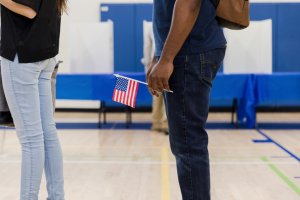 Unrecognizable man holds US flag while waiting to vote