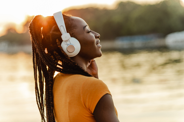 Young African American woman outdoors on sunset and listening music