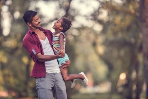 Happy African American father dancing with his cute daughter outdoors.