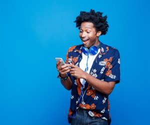 Surprised young man in hawaiian shirt holding smart phone