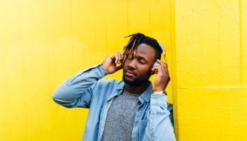 Young man listening music through headphones by yellow wall
