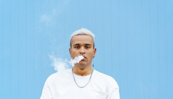 Horizontal portrait of skater hispanic man on his 20s smoking outdoors on blue wall