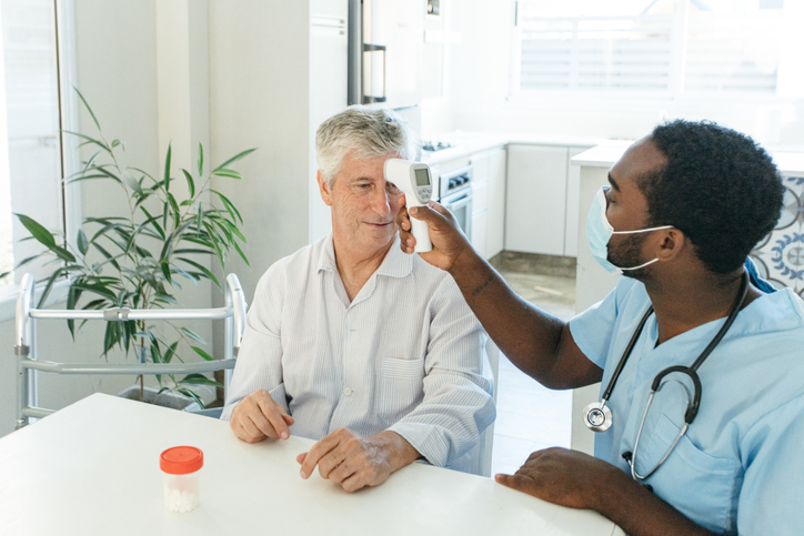 Nurse taking temperature to senior patient at home