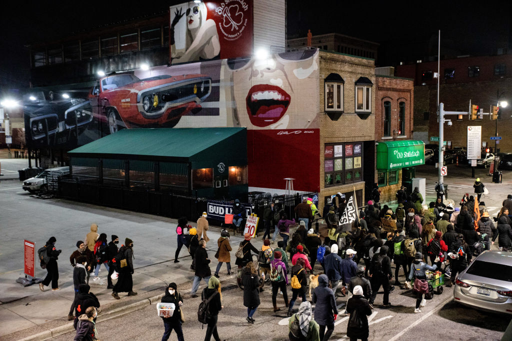 Detroit Will Breathe protesters pass in front of murals in...