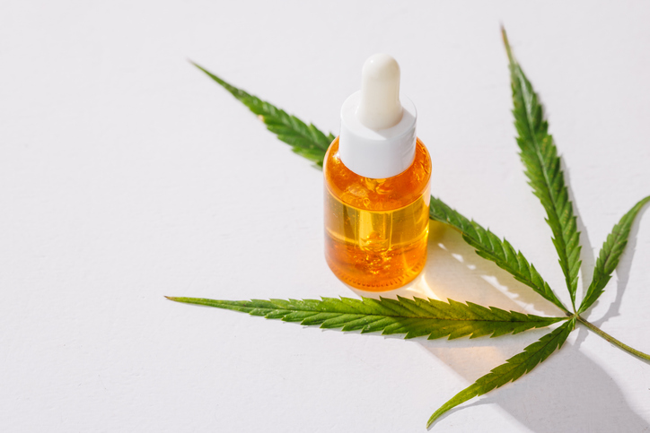 dropper bottle filled with cannabis oil on a marijuana leaf background on a white background