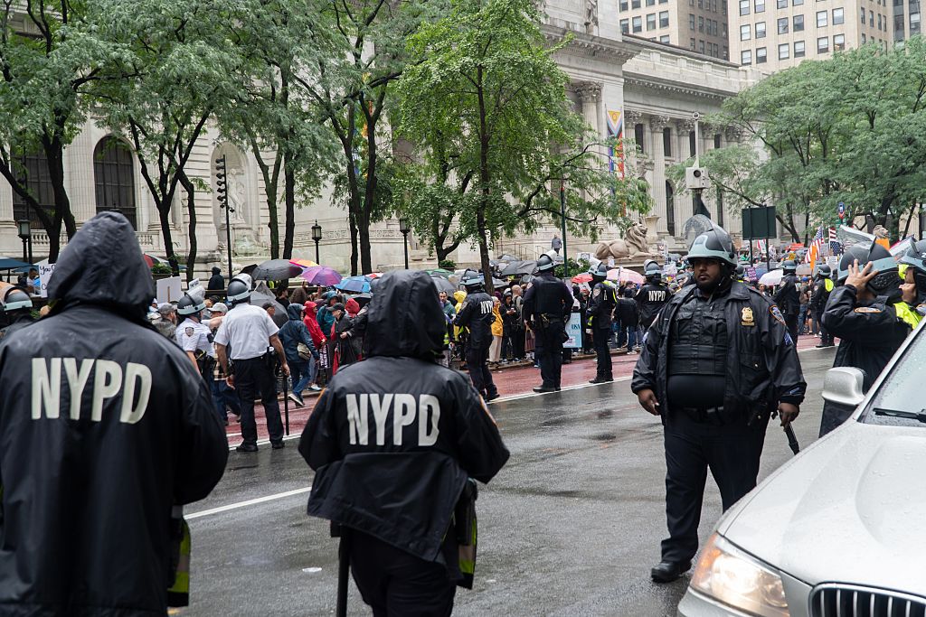 15 NYPD officers, wearing riot helmets with raised visors, line both sides of Fifth Avenue before a large No Kings march, Manhattan, New York City